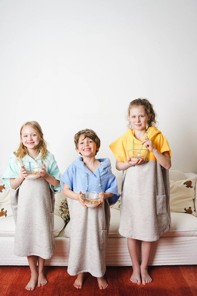 Kinder tragen Badeponchos aus Frottee in verschiedenen Farben zu Hause